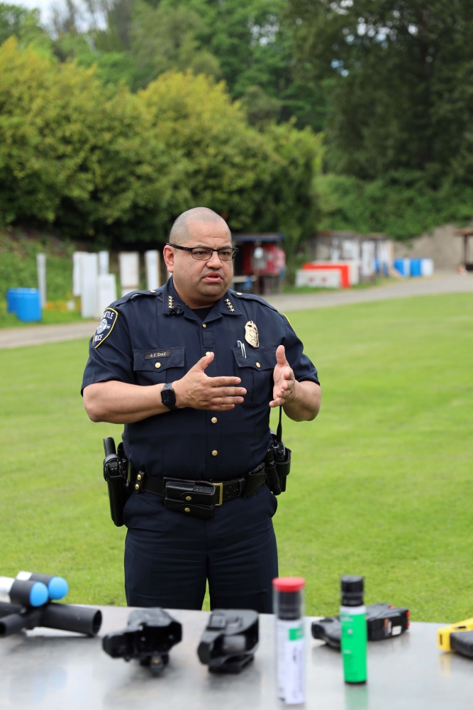 Police chief Adrian Diaz stands talking and gesturing at table arrayed with weapons equipment