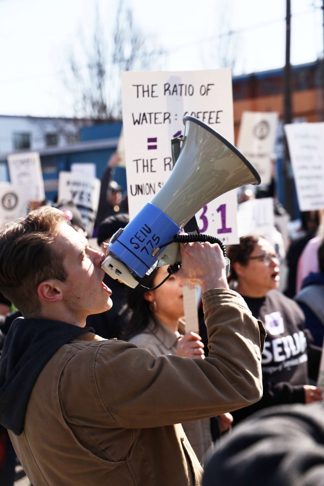 Young white man chants into a microphone emblazoned with an SEIU 775 sticker.