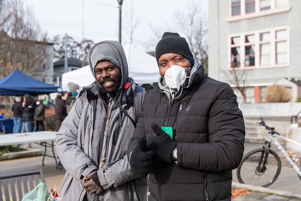 Two black men in hats and new coats stand next to each other.