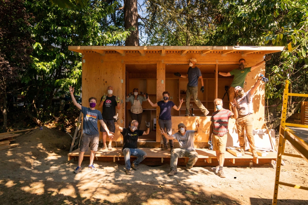 Group of ten people striking celebratory poses in and around a half-finished wooden home