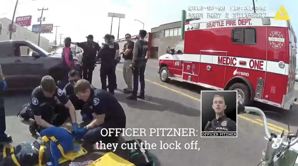 Video still image of medics tending to injured person on ground, with Seattle Fire Department vehicle in background. Photo inset shows young blond Officer Pitzner.