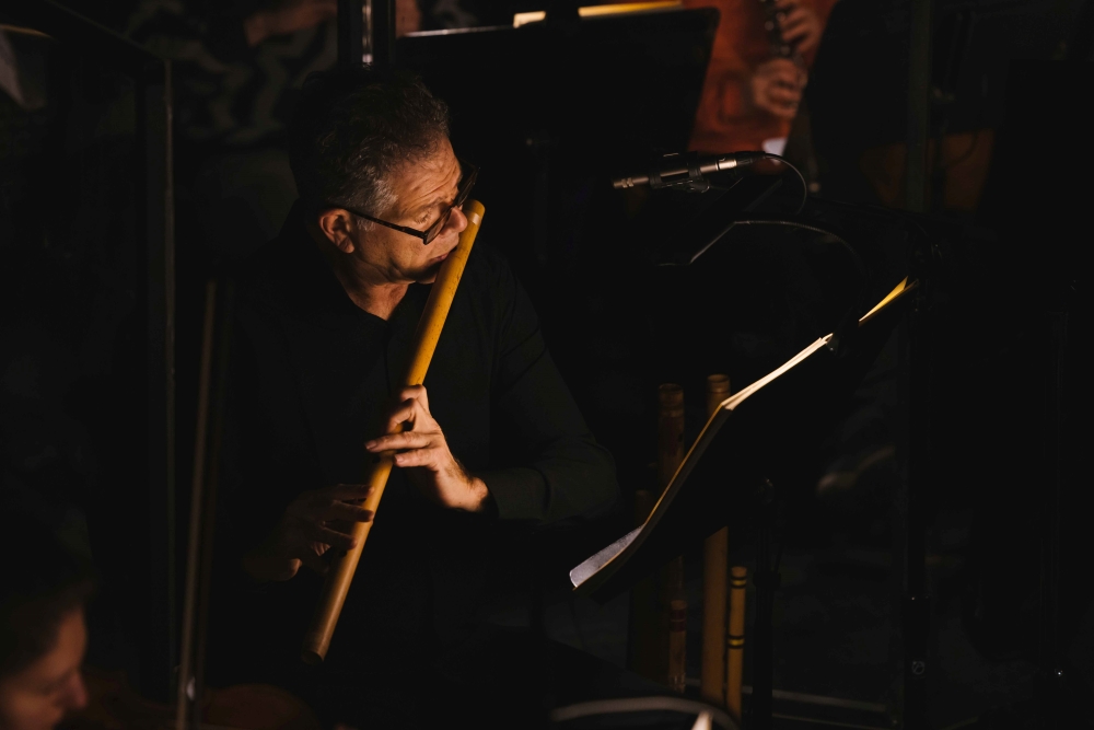 Man in glasses plays long, cylindrical wind instrument.