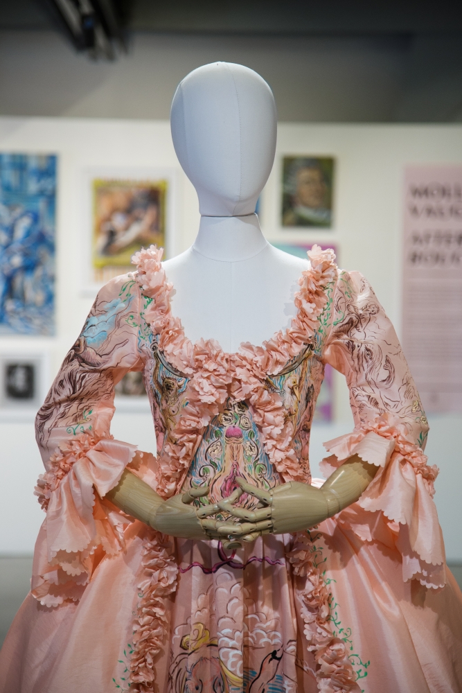 A faceless mannequin wearing 18th-century style pink-and-green dress with frilly cuffs at neck and wrists.