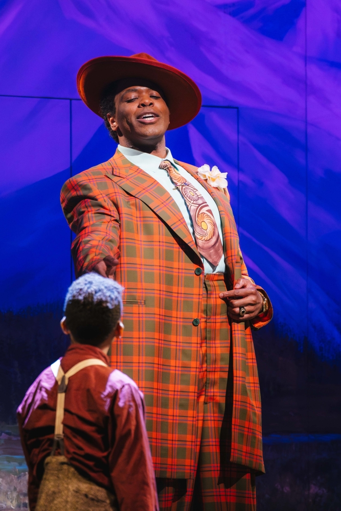 A Black man in an orange suit speaks to a Black boy in “X: The Life and Times of Malcolm X” at Seattle Opera.